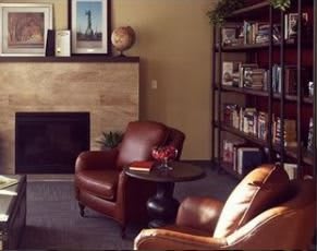 A cozy living room with leather armchairs, a fireplace, and a well-stocked bookshelf.