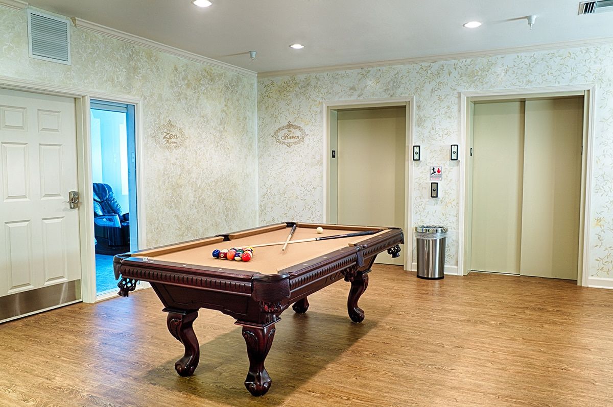 A game room with a pool table situated between two elevators on a wooden floor.