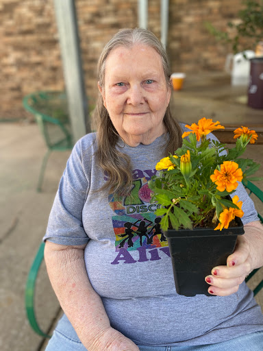 An elderly woman holding a potted flower, enjoying a sunny day outdoors.