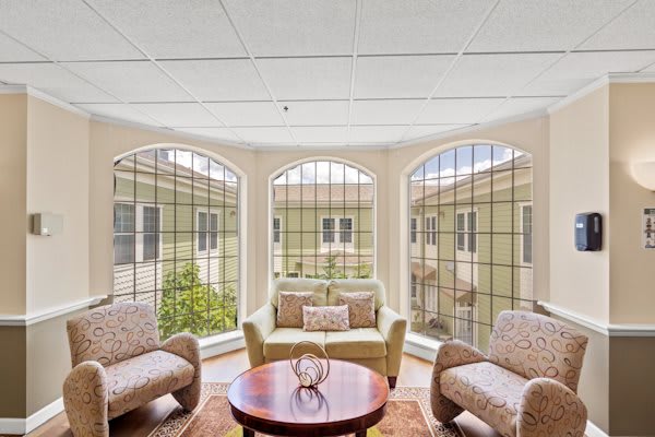 A bright and cozy living room with large arched windows, featuring comfortable seating and a round wooden table.