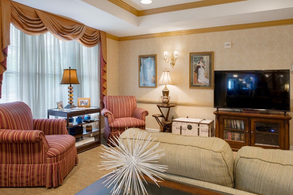 A cozy living room with classic decor, featuring armchairs, a coffee table, and a flat-screen TV.