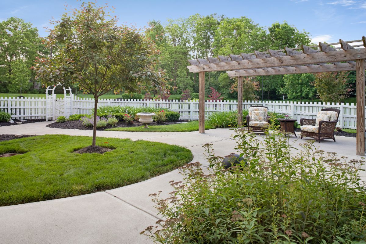 A beautiful garden with a pergola, surrounded by lush greenery and a white picket fence.