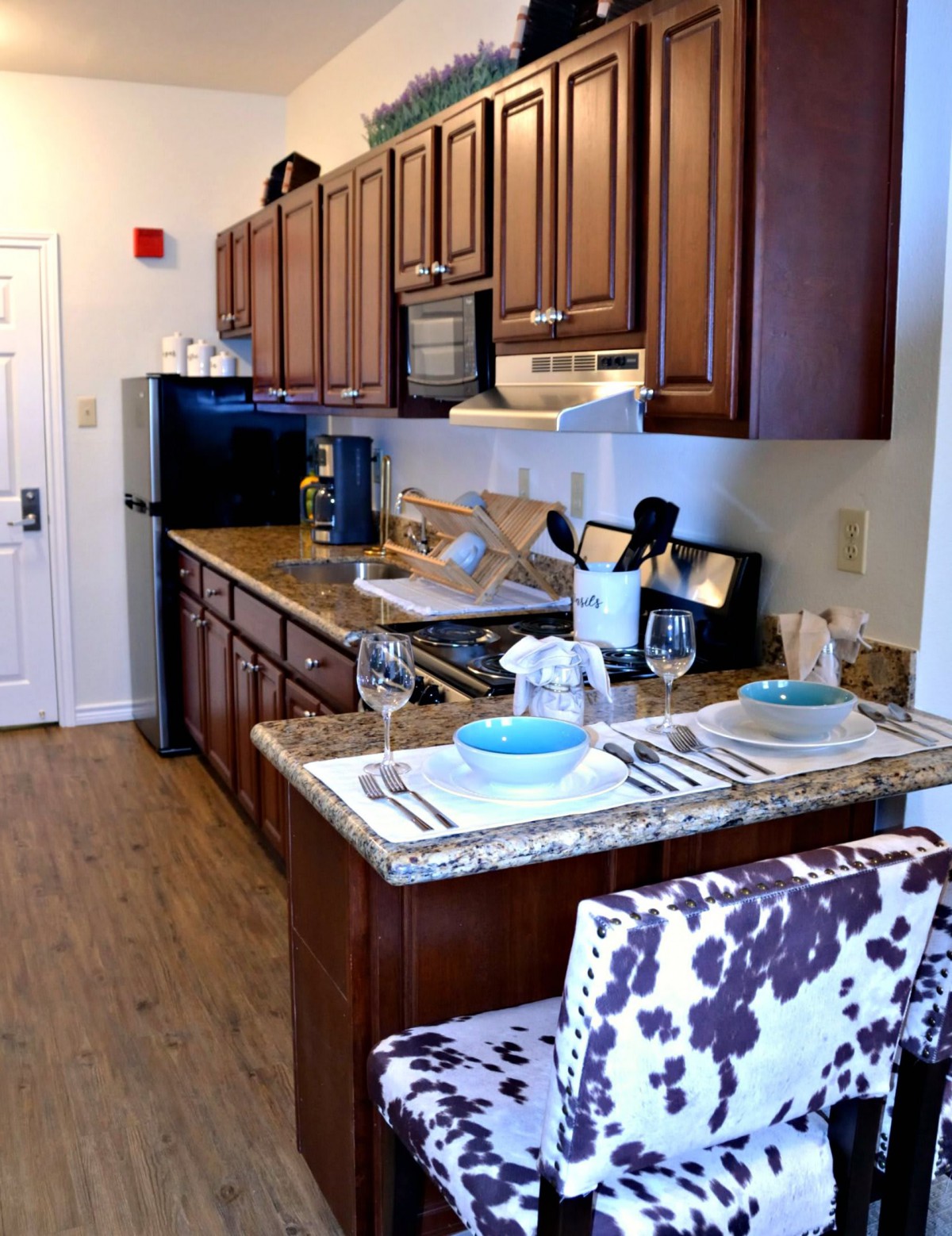 A modern kitchen and dining area featuring a granite countertop with bar seating, wood cabinetry, and stylish decor.