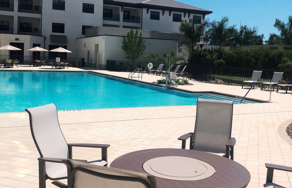 A sunny day at a residential swimming pool with lounge chairs and apartment buildings in the background.