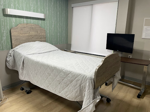 A hospital patient room featuring a bed, television, and window shades.