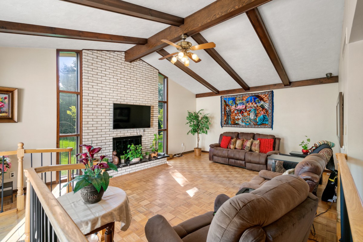A cozy living room featuring exposed wooden beams, a brick fireplace, and comfortable seating.