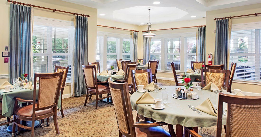 A well-lit dining room with neatly arranged tables and chairs, featuring large windows and elegant decor.