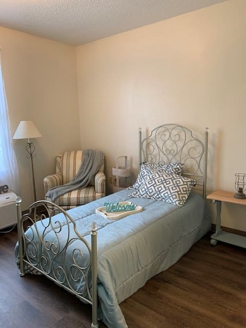 A cozy bedroom with a single metal framed bed, striped armchair, and soft lighting.