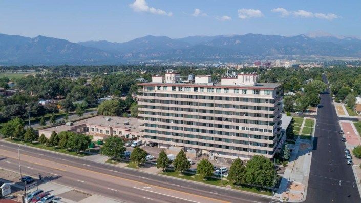 Aerial view of a multi-story building with mountains in the background and a road in the foreground.