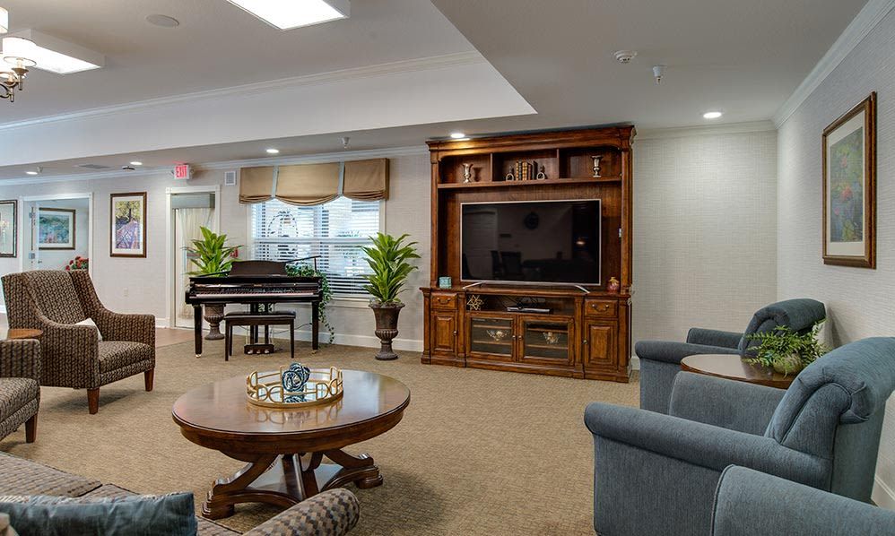 A cozy living room featuring a television set in a wooden cabinet, a grand piano, and a round coffee table surrounded by comfortable seating.
