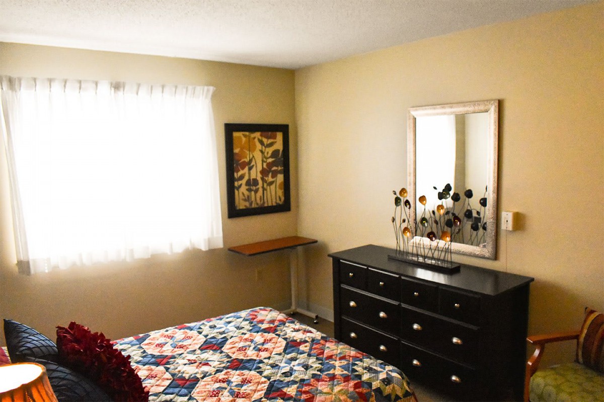 A cozy bedroom with a floral bedspread, dresser, and wall decor.