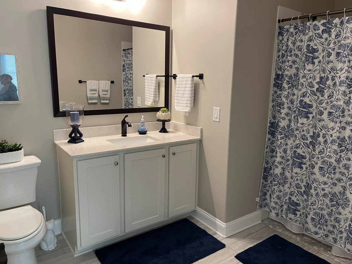 A modern bathroom featuring a mirror above a vanity with a sink, flanked by towels and a patterned shower curtain.