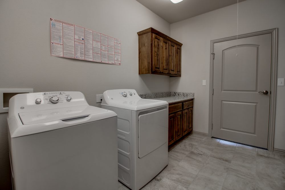 A laundry room with a washing machine, dryer, and wooden cabinets.