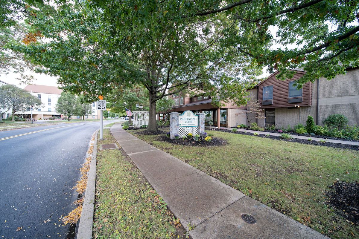 A quiet suburban street with a sidewalk, trees, and residential houses.