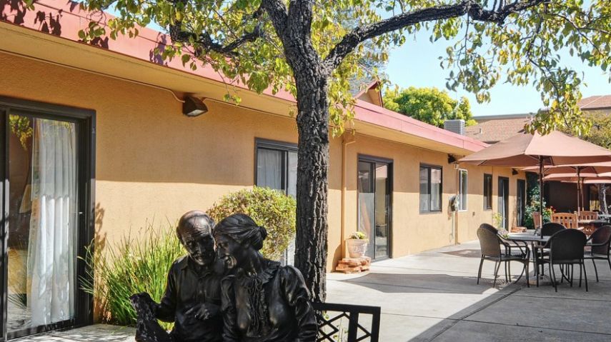 A sculpture of two people sitting on a bench under a tree outside a building.