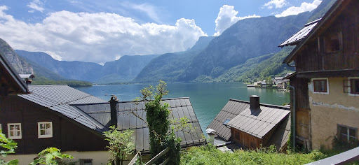 A tranquil lakeside view surrounded by majestic mountains and charming houses under a bright sky.
