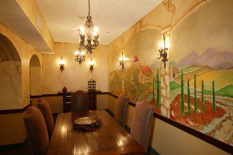 A warmly lit dining room with a mural on the wall and a chandelier overhead.