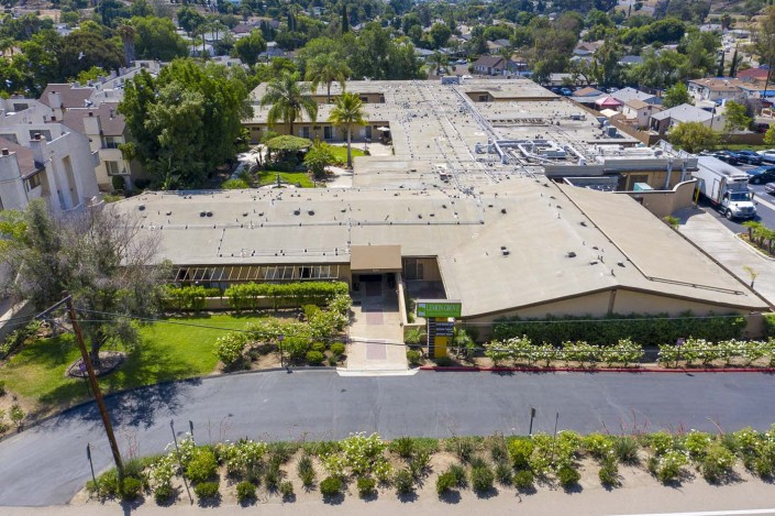 Aerial view of a large building complex with landscaped gardens and a parking lot in a suburban area.