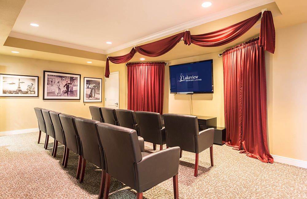 A cozy theater room with rows of seating and a large screen, accented by red curtains and framed pictures on the walls.