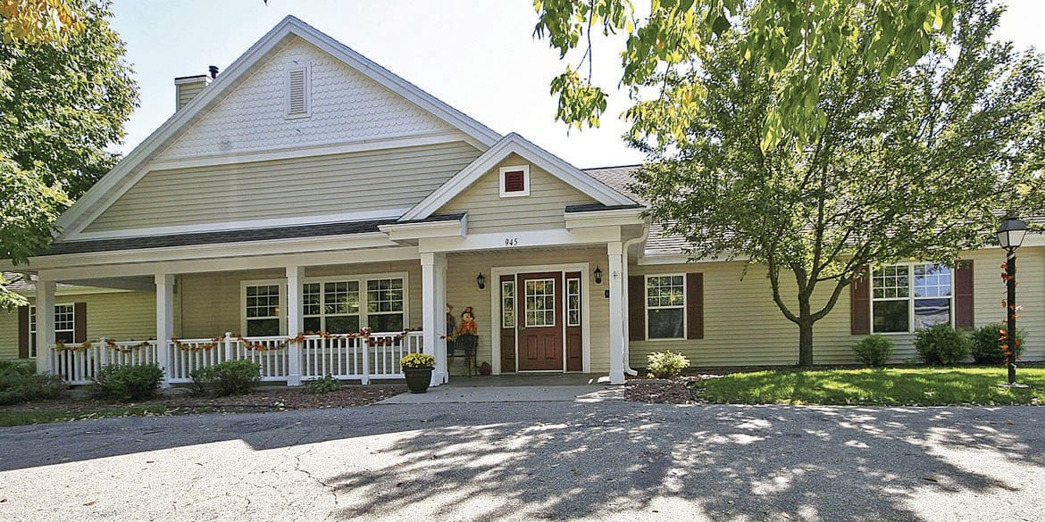 A charming residential house with a spacious porch and surrounding trees.