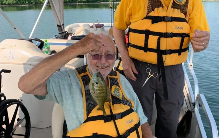 A person on a boat proudly holding up a fish they caught, while wearing a life jacket.