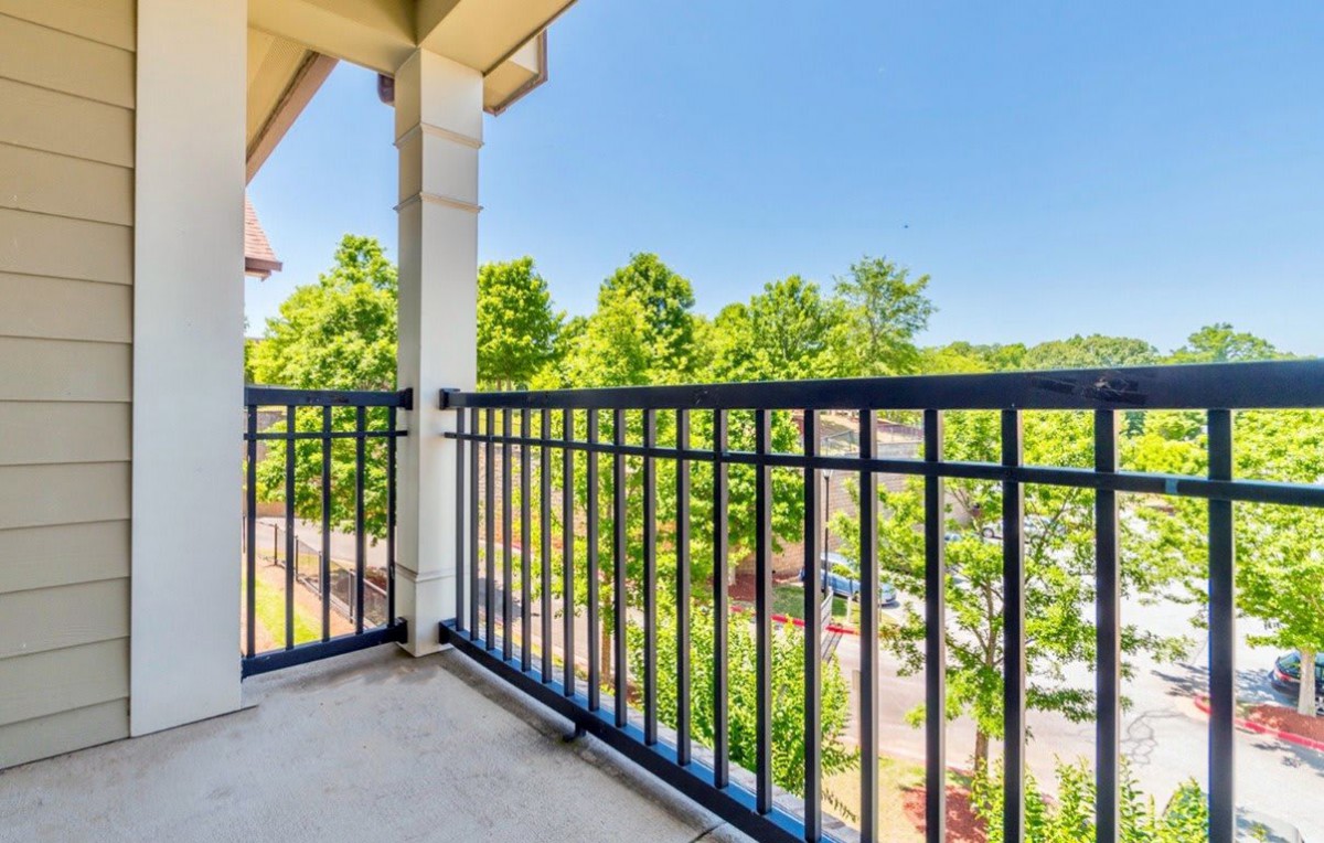 A sunny view from a balcony with blue railings and lush green trees in the background.