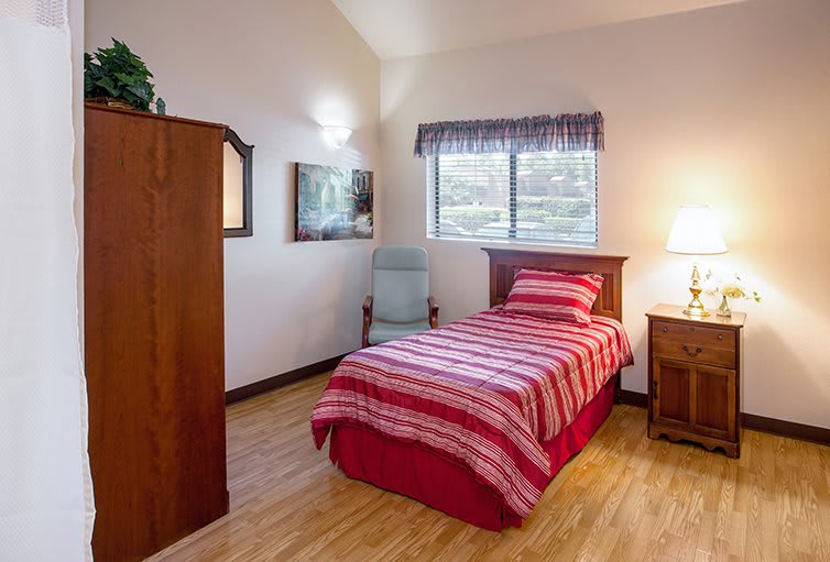 A cozy bedroom with a single bed featuring striped bedding, a wooden dresser, and a nightstand with a lamp beside it.