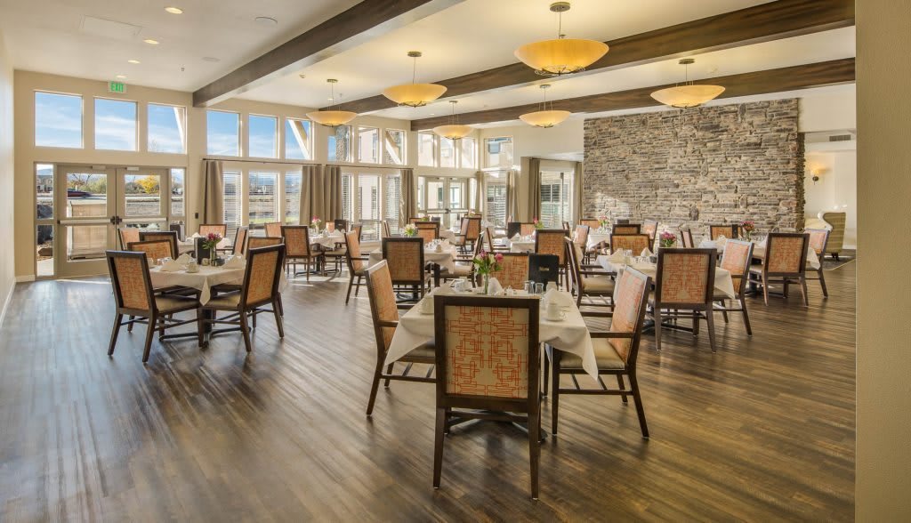 A spacious and elegantly decorated dining room with neatly arranged tables and chairs, featuring large windows and soft lighting.
