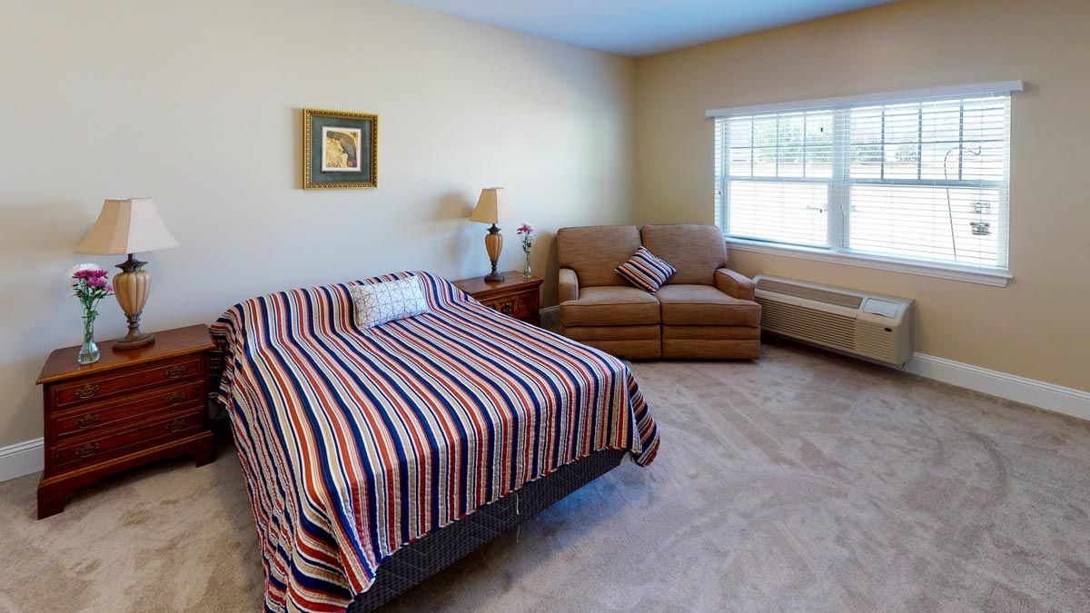 A cozy bedroom with a striped bedspread, an armchair, and a window.