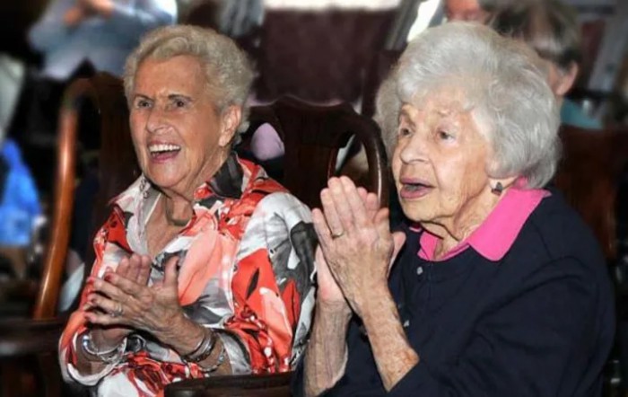 Two elderly women clapping and smiling, enjoying a joyful moment together.