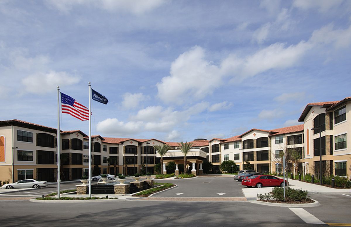 A large building with American and company flags, featuring a parking lot and landscaping under a cloudy sky.