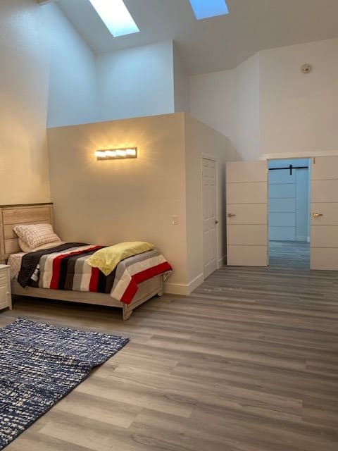 A modern, minimalist bedroom with a single bed featuring striped bedding and a cozy rug on a wooden floor.