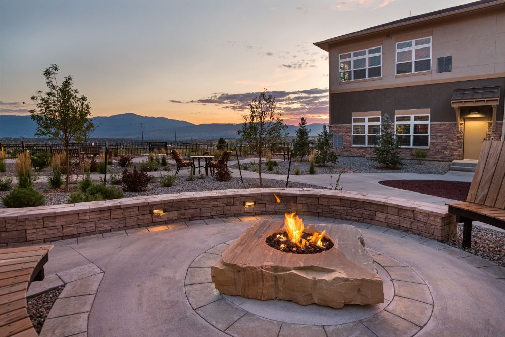 A scenic outdoor patio with a fire pit at sunset, overlooking mountains and adjacent to a building.