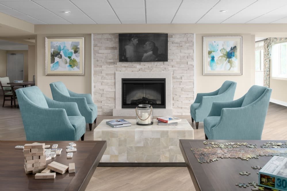 A modern living room with a fireplace, surrounded by blue armchairs, and adorned with artwork and a television.