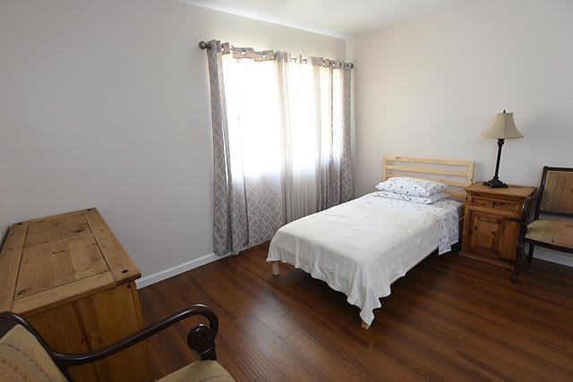 A minimalist bedroom featuring a single bed with white bedding and wooden furniture.