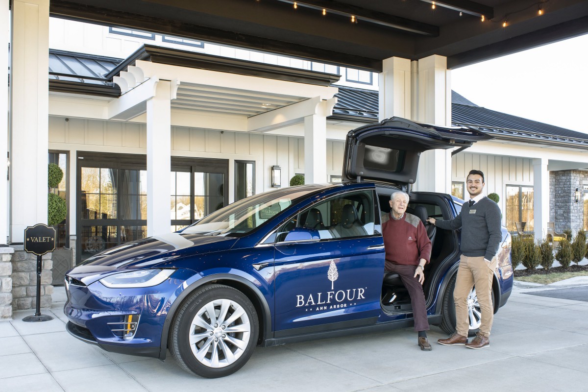 Two people standing next to a Tesla with 'Balfour' branding in front of a building entrance.