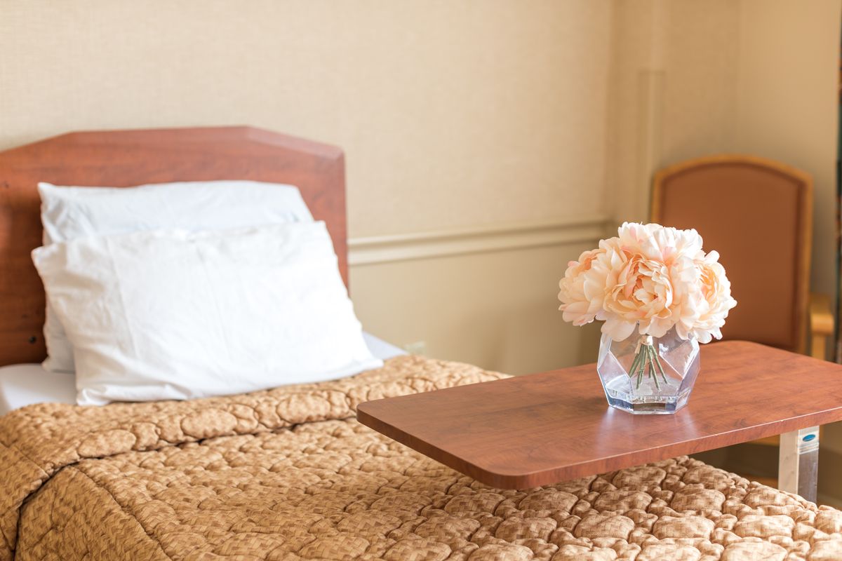 A cozy bedroom with a neatly made bed and a vase of flowers on the side table.