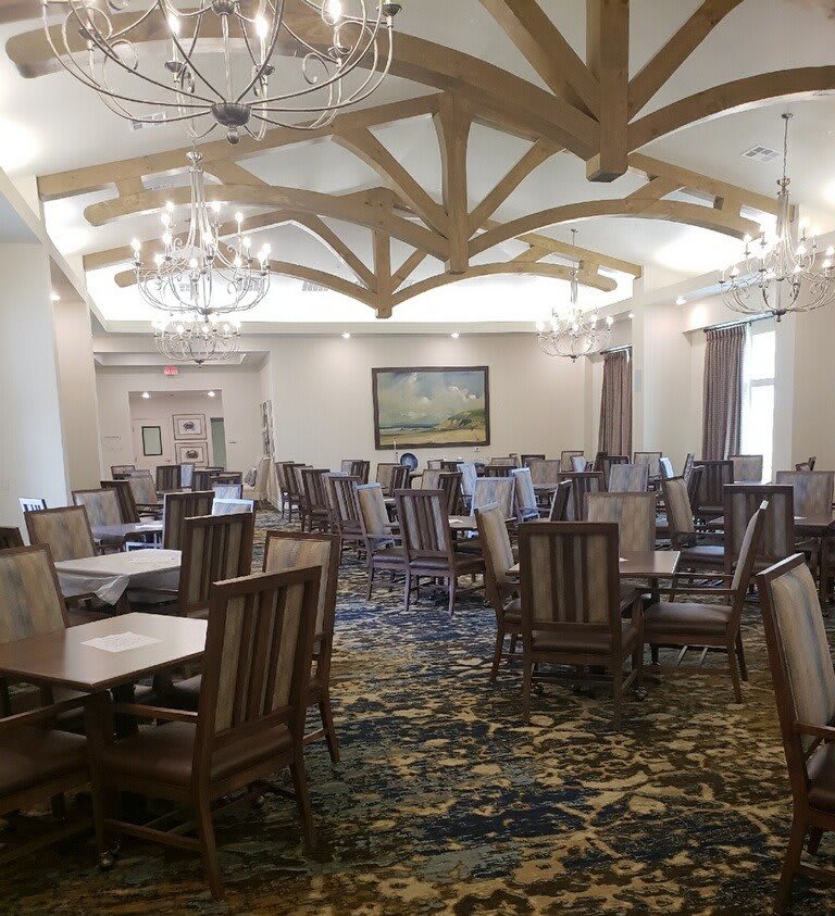 An elegantly designed dining room with multiple wooden tables and chairs, decorated with chandeliers and wooden ceiling beams.