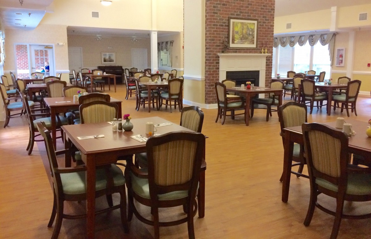 A spacious dining area with several tables and chairs, featuring a cozy fireplace and wooden flooring.