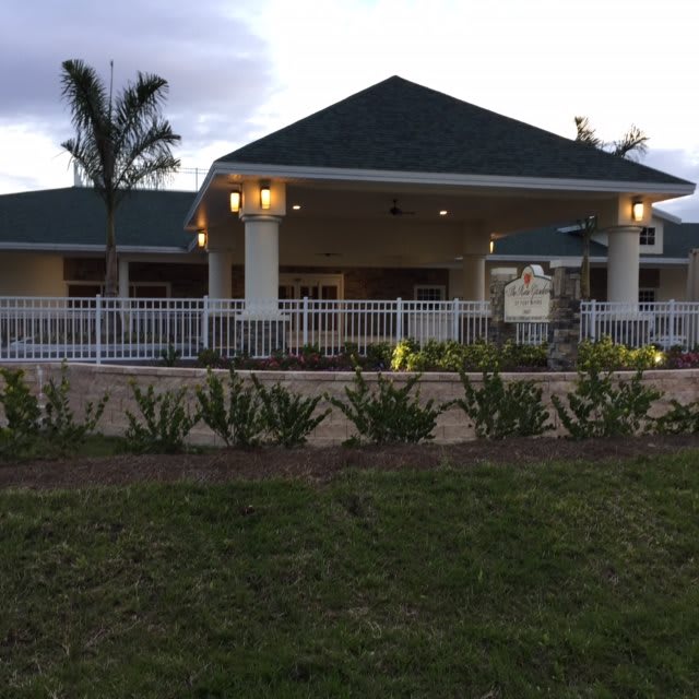 A well-lit building surrounded by landscaped greenery and palm trees in the evening.