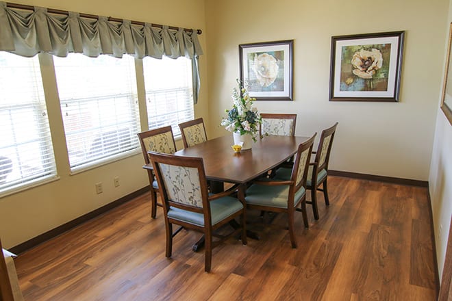A cozy dining room featuring a wooden table and six chairs, adorned with floral decorations and two pieces of artwork on the wall.