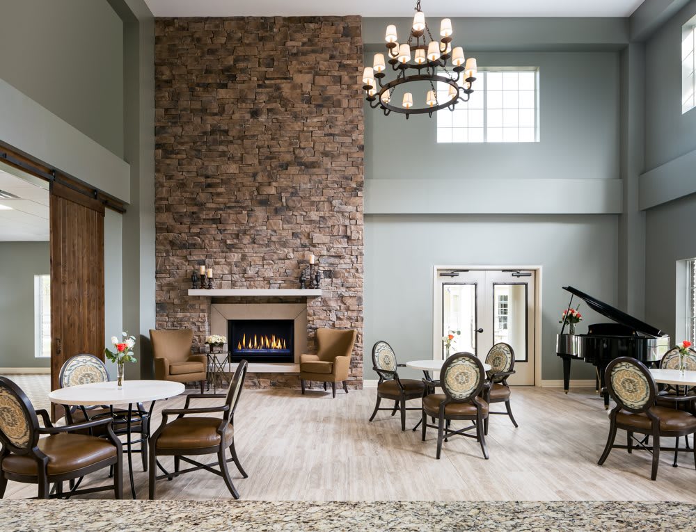 A spacious living room with a tall stone fireplace, elegant chandelier, and grand piano.