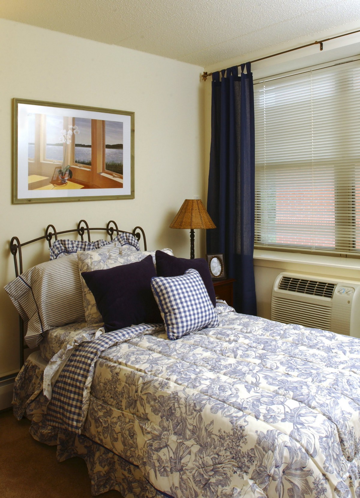 A cozy bedroom with a neatly made bed, decorated pillows, and a framed painting on the wall.