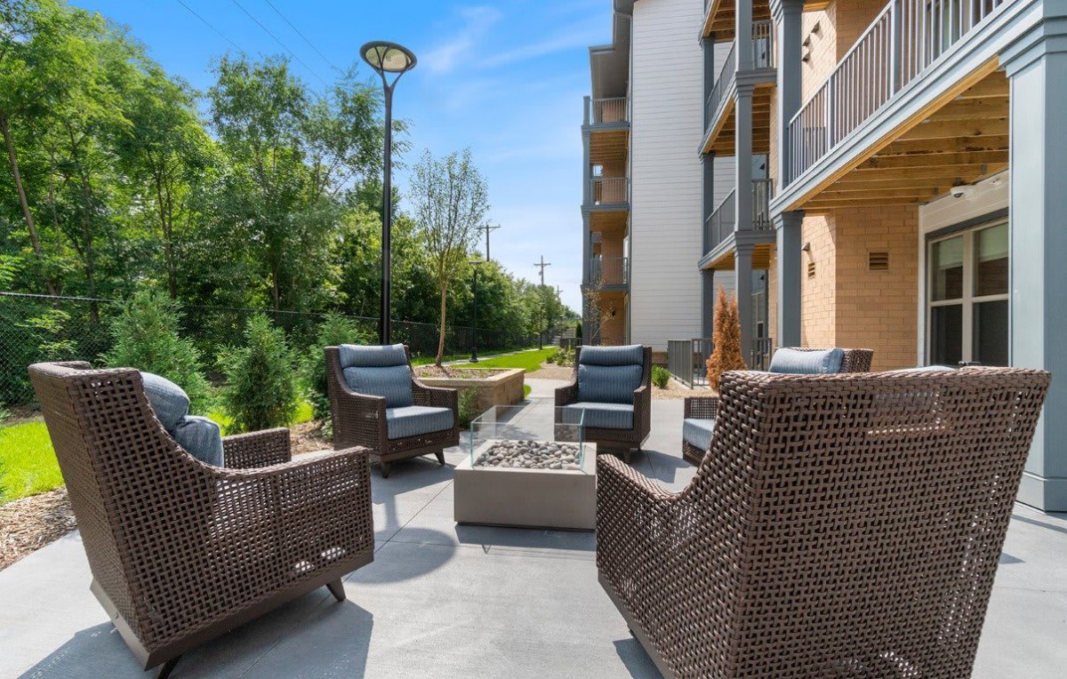 A modern outdoor patio with wicker furniture and a fire pit, situated next to an apartment building.