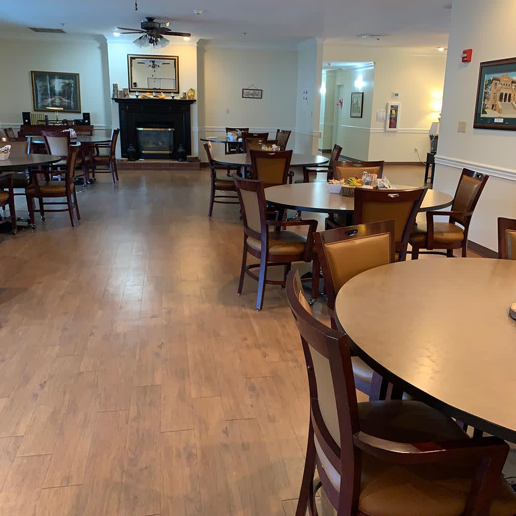 An empty dining room with multiple tables and chairs arranged on a wooden floor.