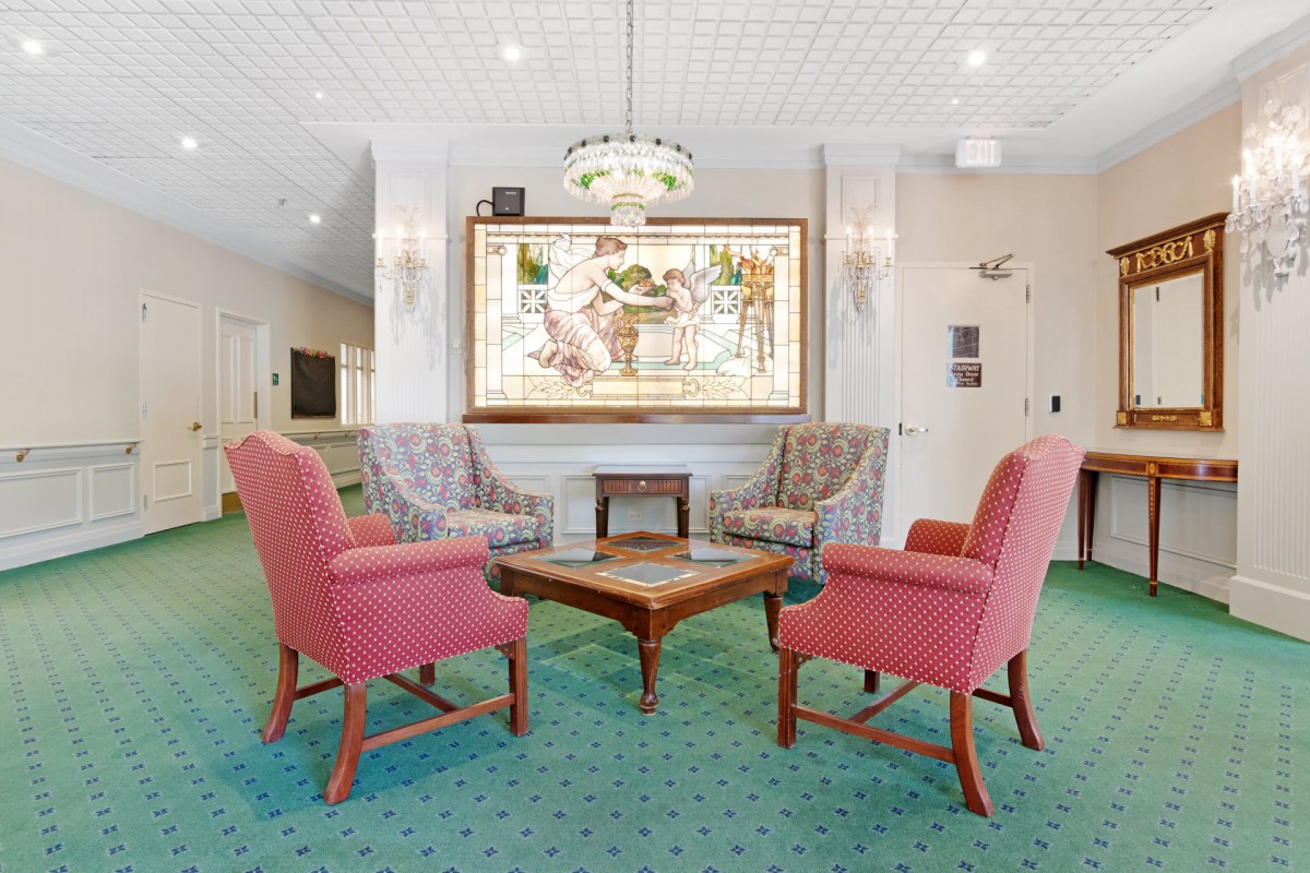 A cozy lobby seating area with red chairs and a coffee table, featuring a large painting on the wall.