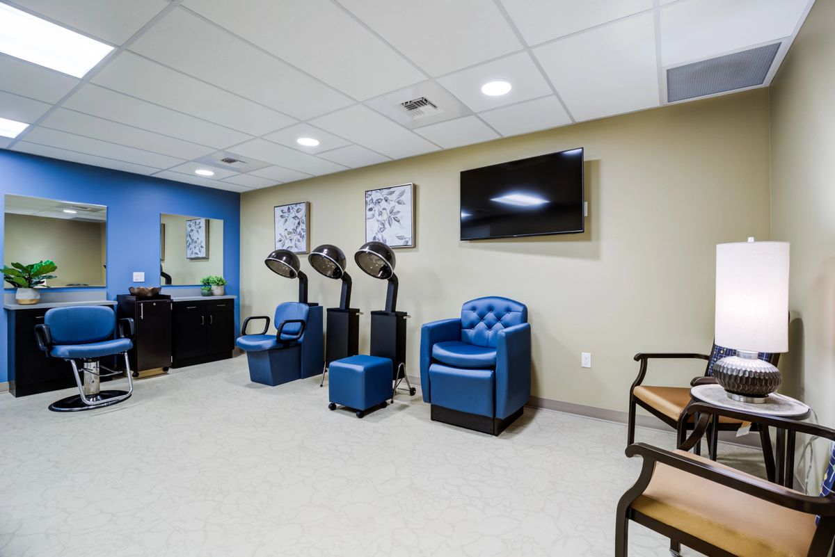 A modern salon interior featuring comfortable chairs, hair dryers, and a television, with blue accents creating a relaxing atmosphere.