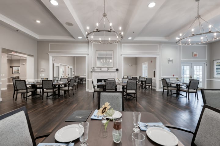 A spacious and elegantly decorated dining room with neatly arranged tables and chairs under a large chandelier.