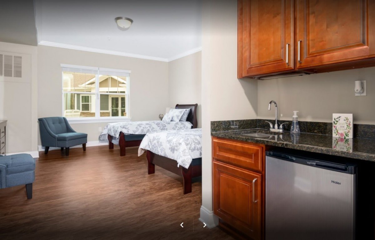 A bright bedroom featuring twin beds, wooden flooring, and a small sink area.