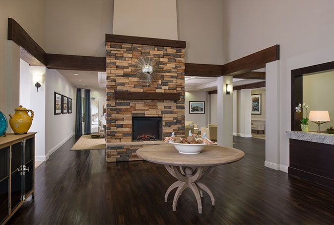 A cozy living room interior featuring a central stone fireplace, hardwood flooring, and a stylish wooden table.